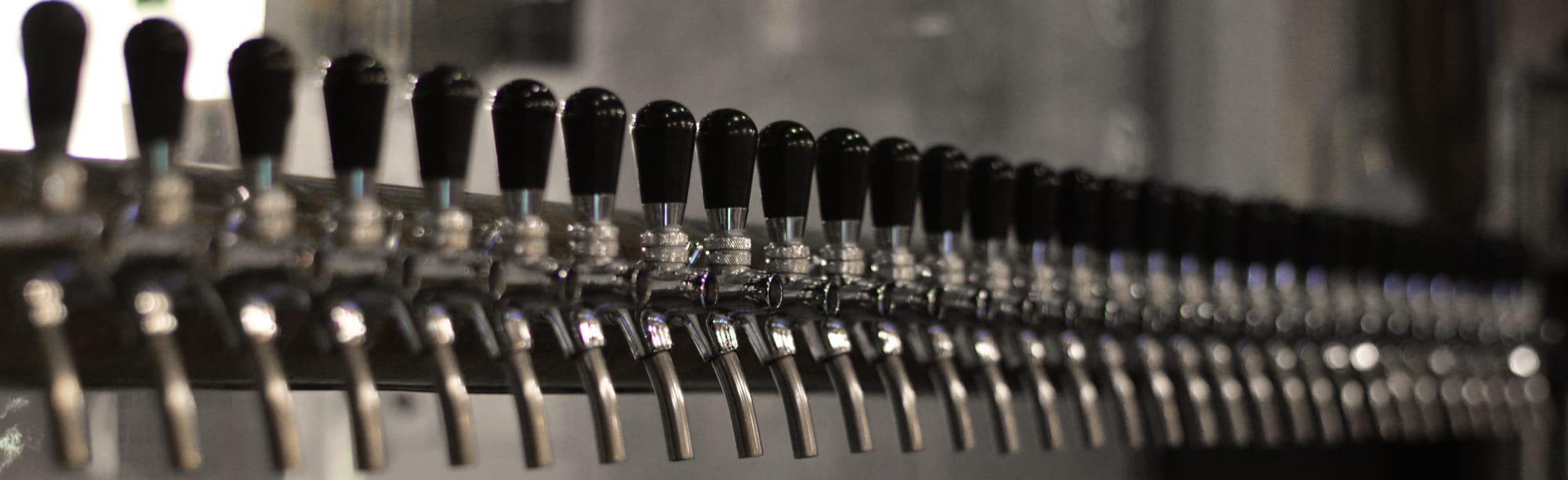 Schattiger Innenbereich der Bierbar „La Mise en Bière“ in Lausanne, Blick auf die Theke mit den 32 Zapfhähnen